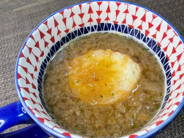 マグカップに注いだオニオングラタンスープ。表面にバゲットとチーズが浮かぶ調理途中