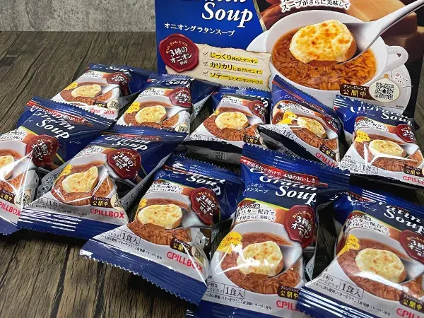 コストコ「PILLBOX オニオングラタンスープ」外箱と個包装10袋をテーブルに並べた全量イメージ
